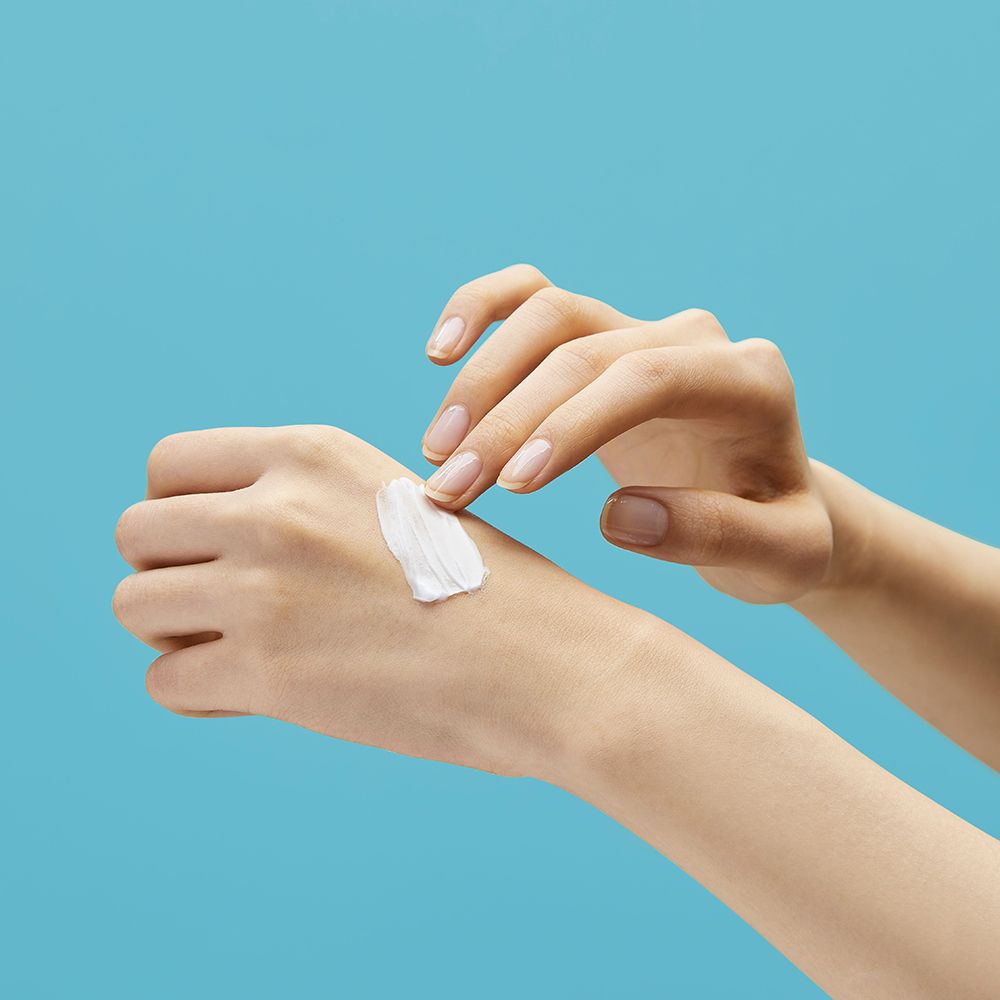 Handen met crème op de huid. Achtergrond: lichtblauw.