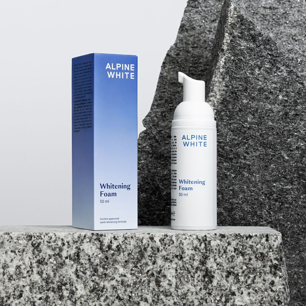 Witte fles en doos met "ALPINE WHITE Whitening Foam". Op steen. 50 ml.