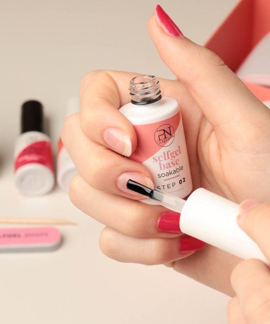 Personne tenant un flacon avec pinceau. Inscription: selfgel base soakable, STEP 02. Logo PN. Lime et bâtonnet.