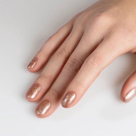 Main avec ongles vernis rose-or. Fond blanc.