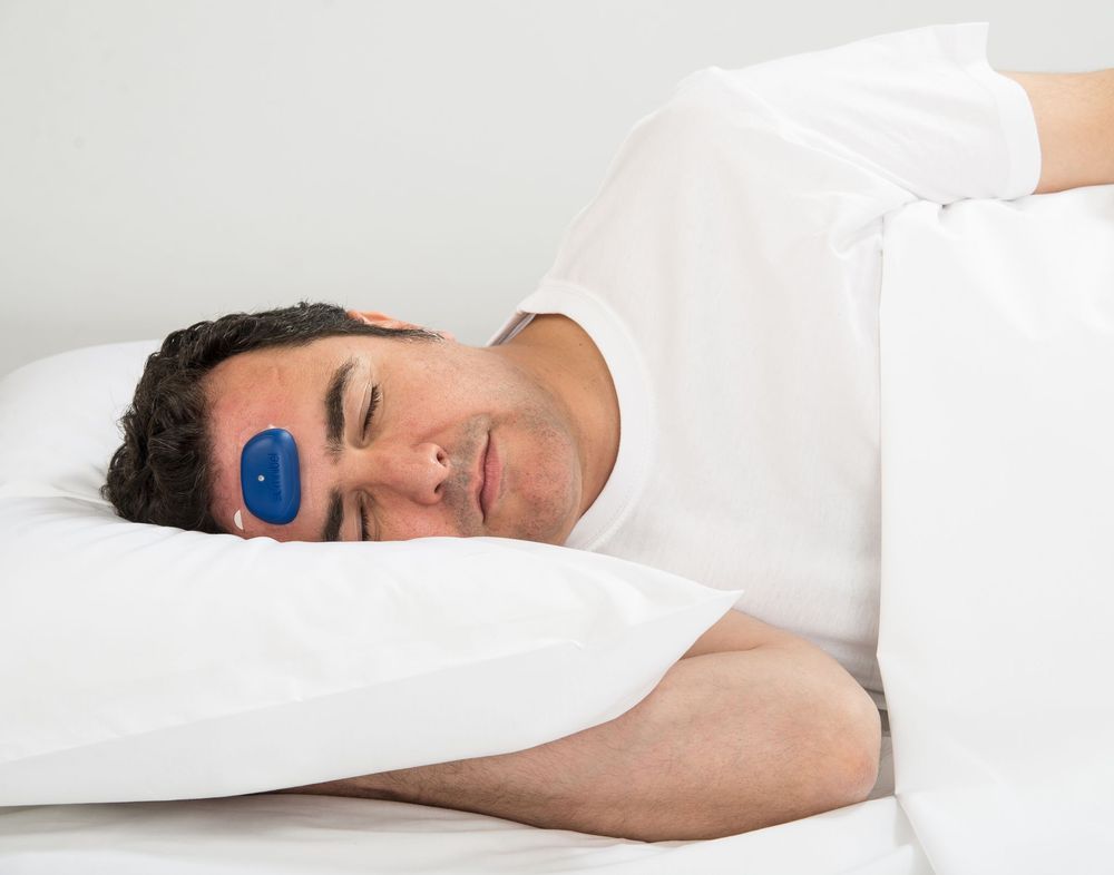 Homme au lit avec appareil bleu sur le front. Couché sur un oreiller.