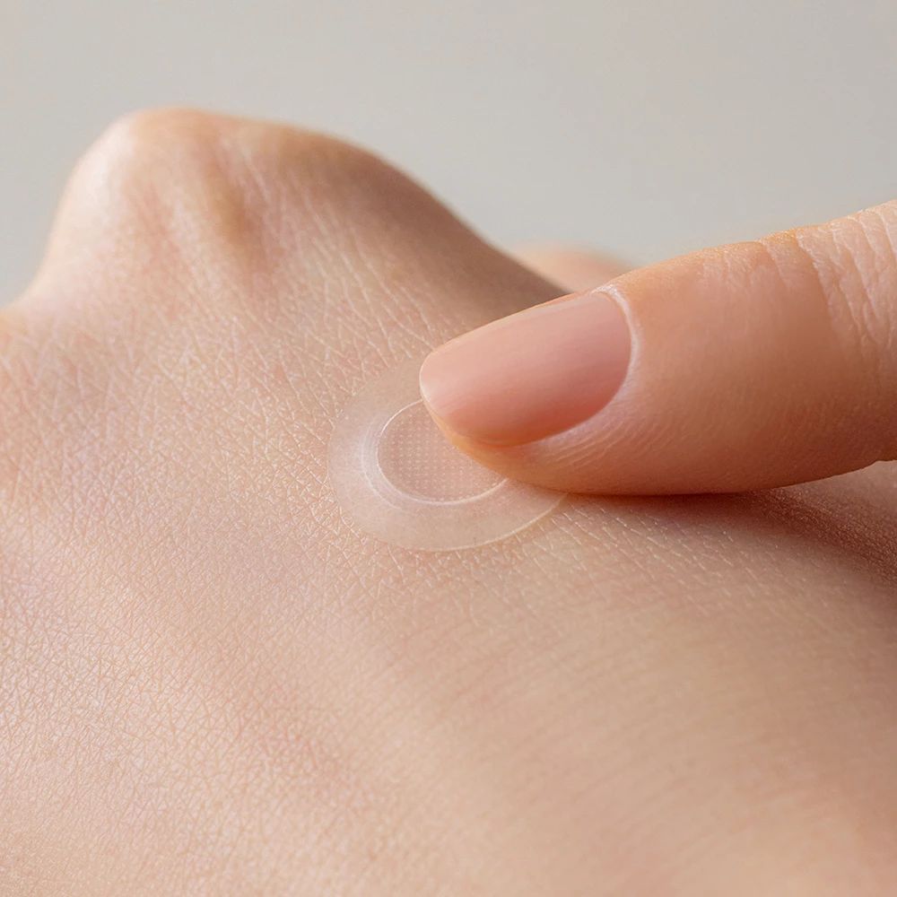 Een vinger plaatst een transparante, ronde patch op de huid. Close-up van een hand.