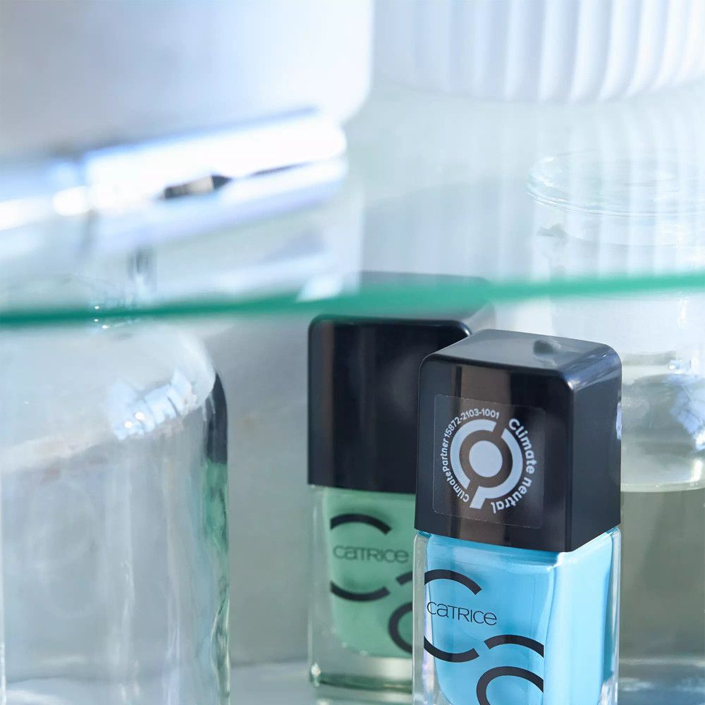 Deux flacons de vernis à ongles, un bleu, un vert, sur une étagère. Catrice sur les flacons. Logo Climate Partner.