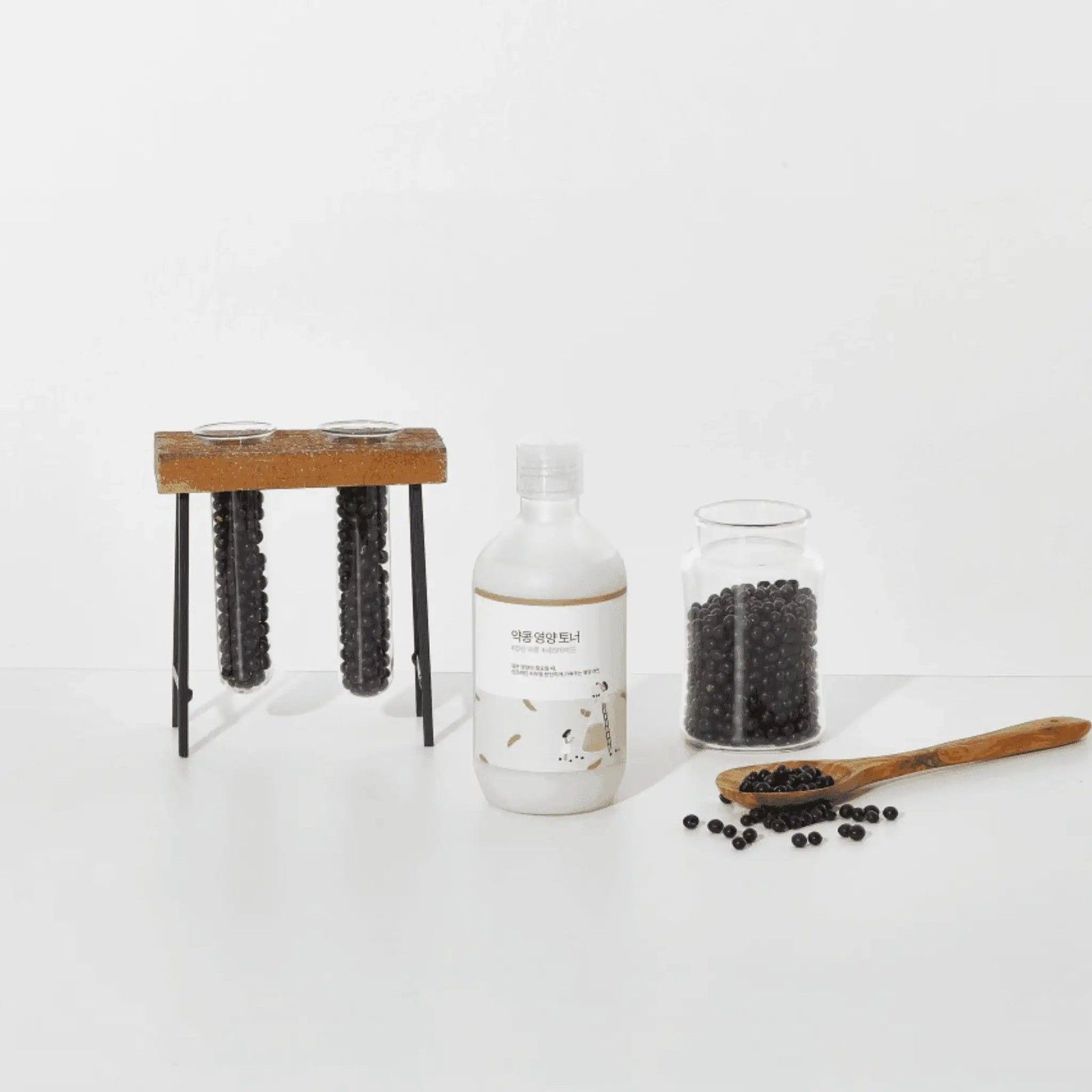 Fles ROUND LAB Soy Bean Nourishing Toner naast een pot met sojabonen en een houten lepel.