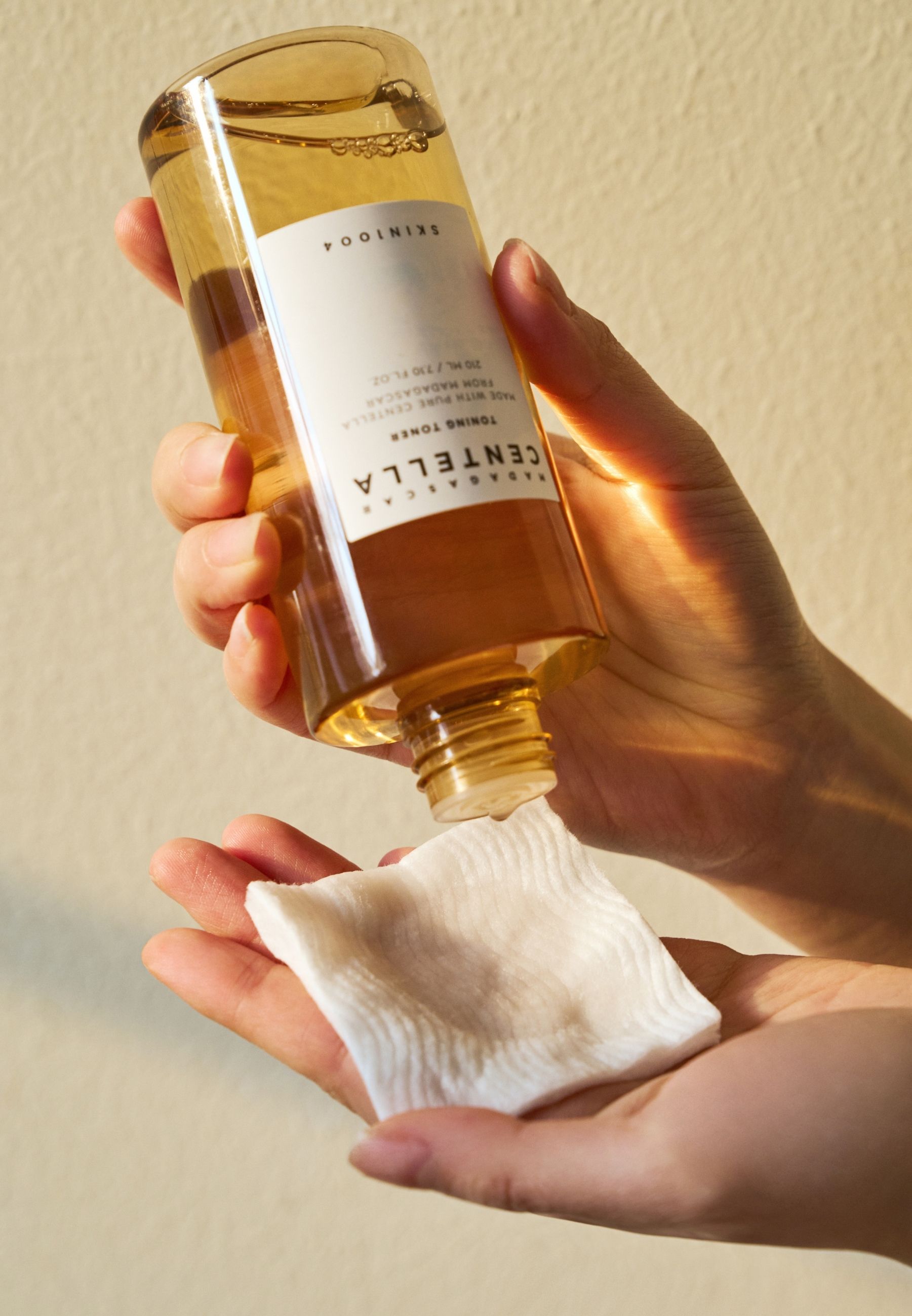 Handen houden fles en wattenschijfje vast. Toner wordt op het schijfje gegoten.