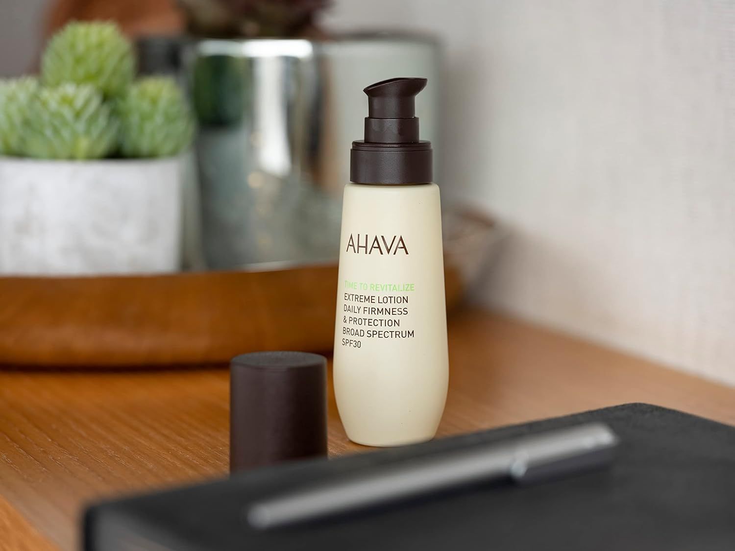Ahava T.T.R. Extreme Lotion SPF30 op een houten tafel naast een notitieboek en pen.
