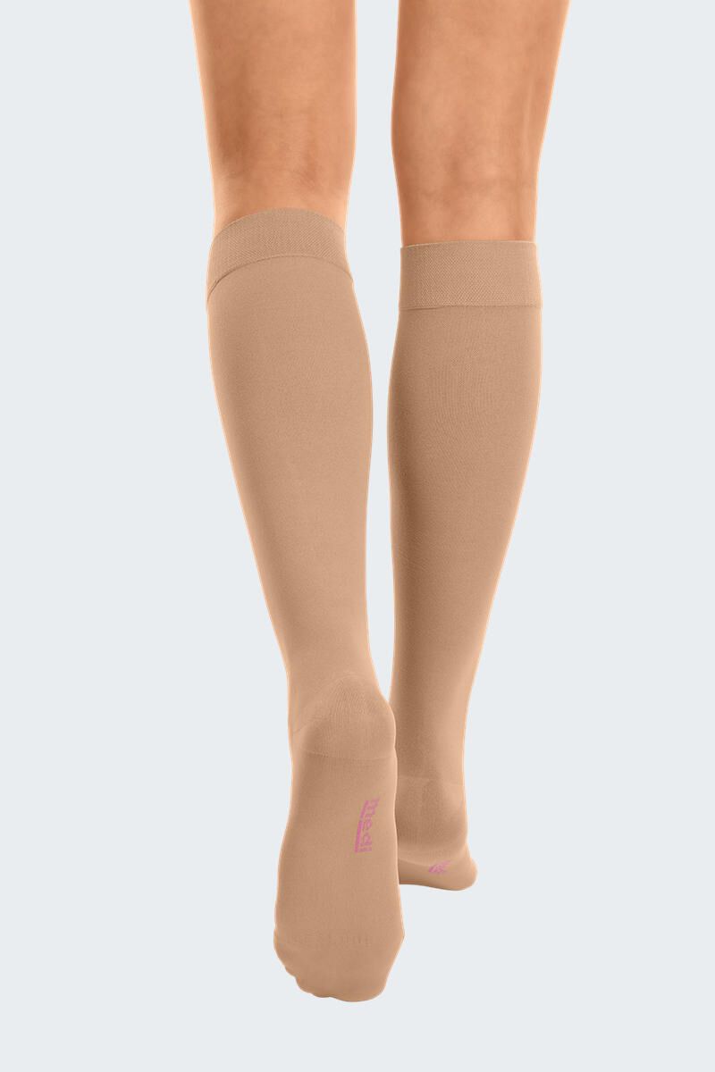 Bas de compression couleur chair, montants jusqu'aux genoux, portés sur les jambes. Vue arrière. Zone des orteils avec texte.