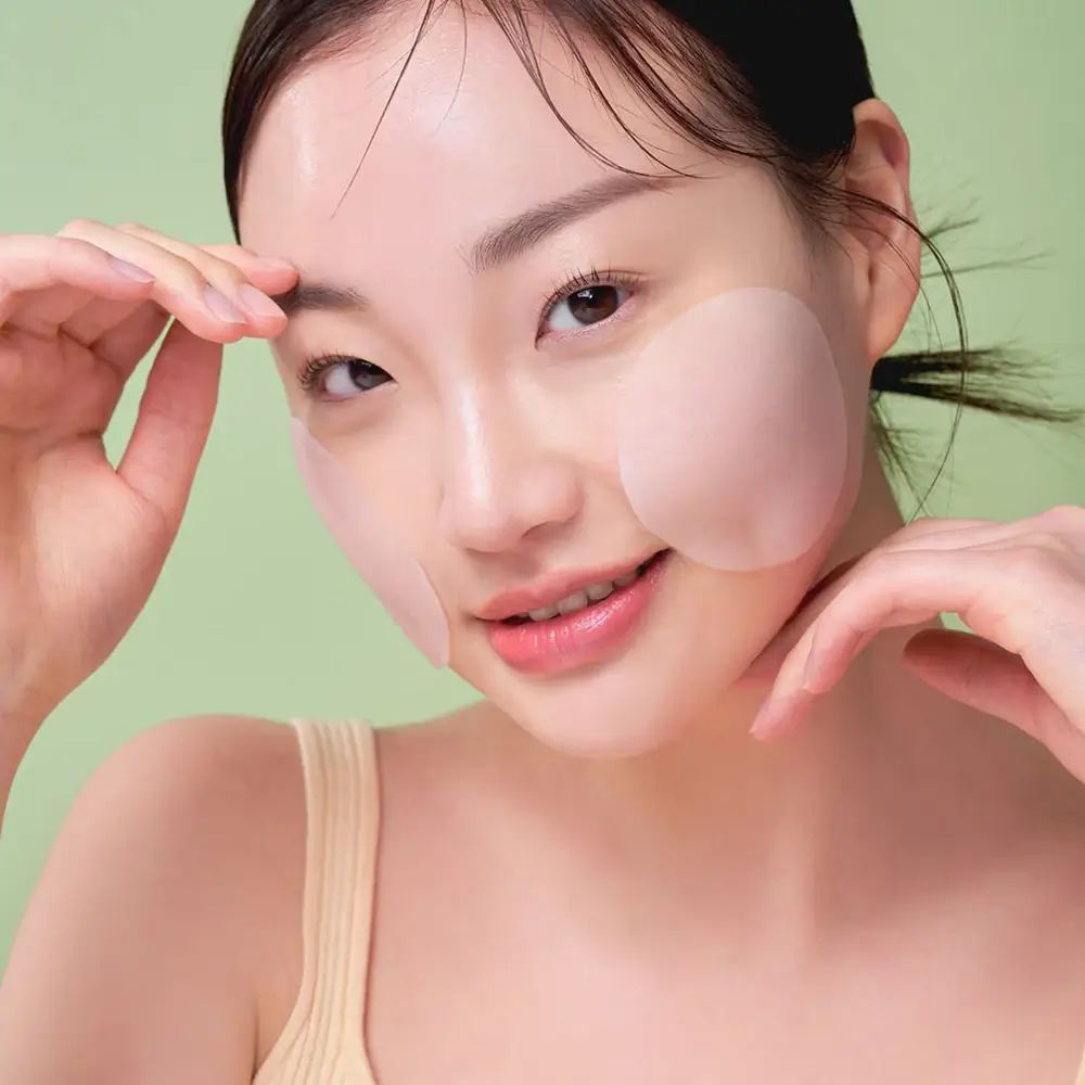 Vrouw met pads op wangen. Pads zijn rond en transparant. Groene achtergrond.