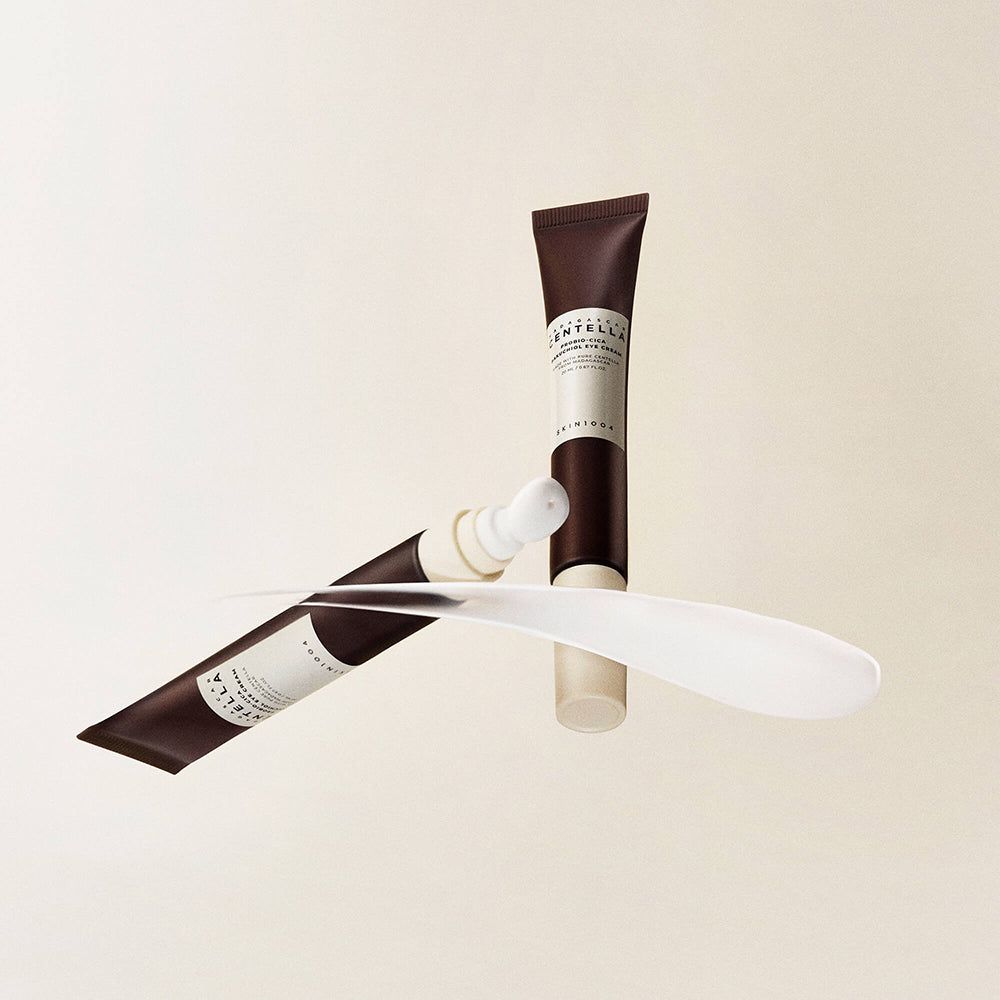 Oogcrèmetube en spatel. Tube bruin-wit met opschrift. Spatel wit. Productnaam onleesbaar.