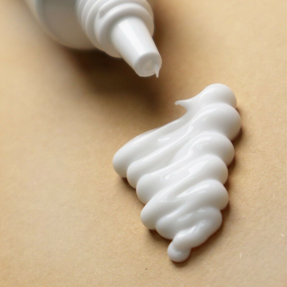 Close-up van witte oogcrème die uit een tube wordt geperst. Crème heeft een golvende vorm.