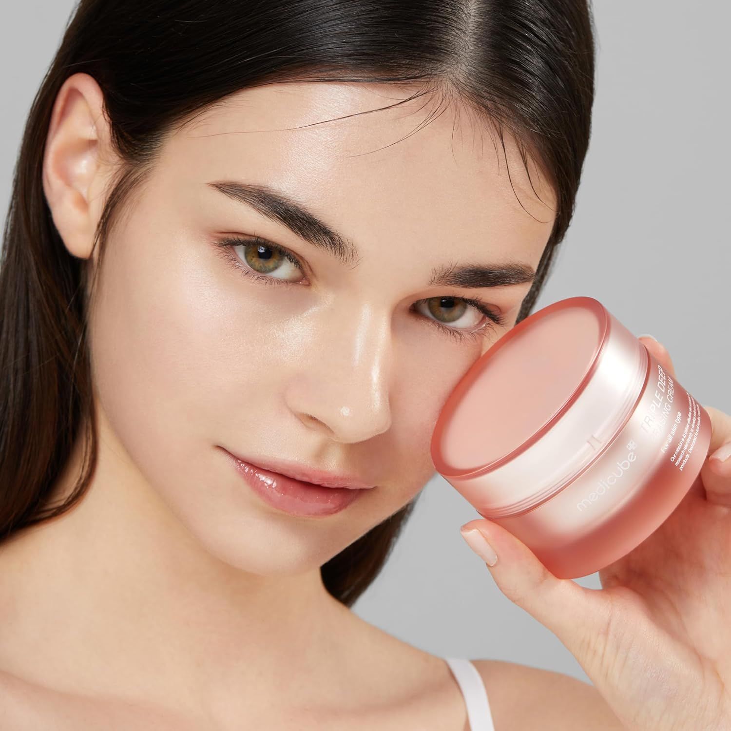 Femme tenant un pot de crème rose. Inscription: Triple Deep Erasing Cream. Marque: Medicube. Produit de soin de la peau.