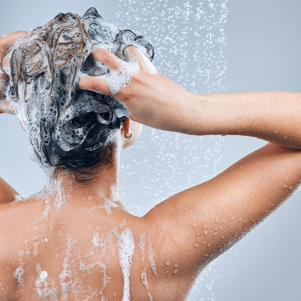 Personne se lave les cheveux sous la douche. Mousse sur la tête et le dos. Jets d'eau visibles.