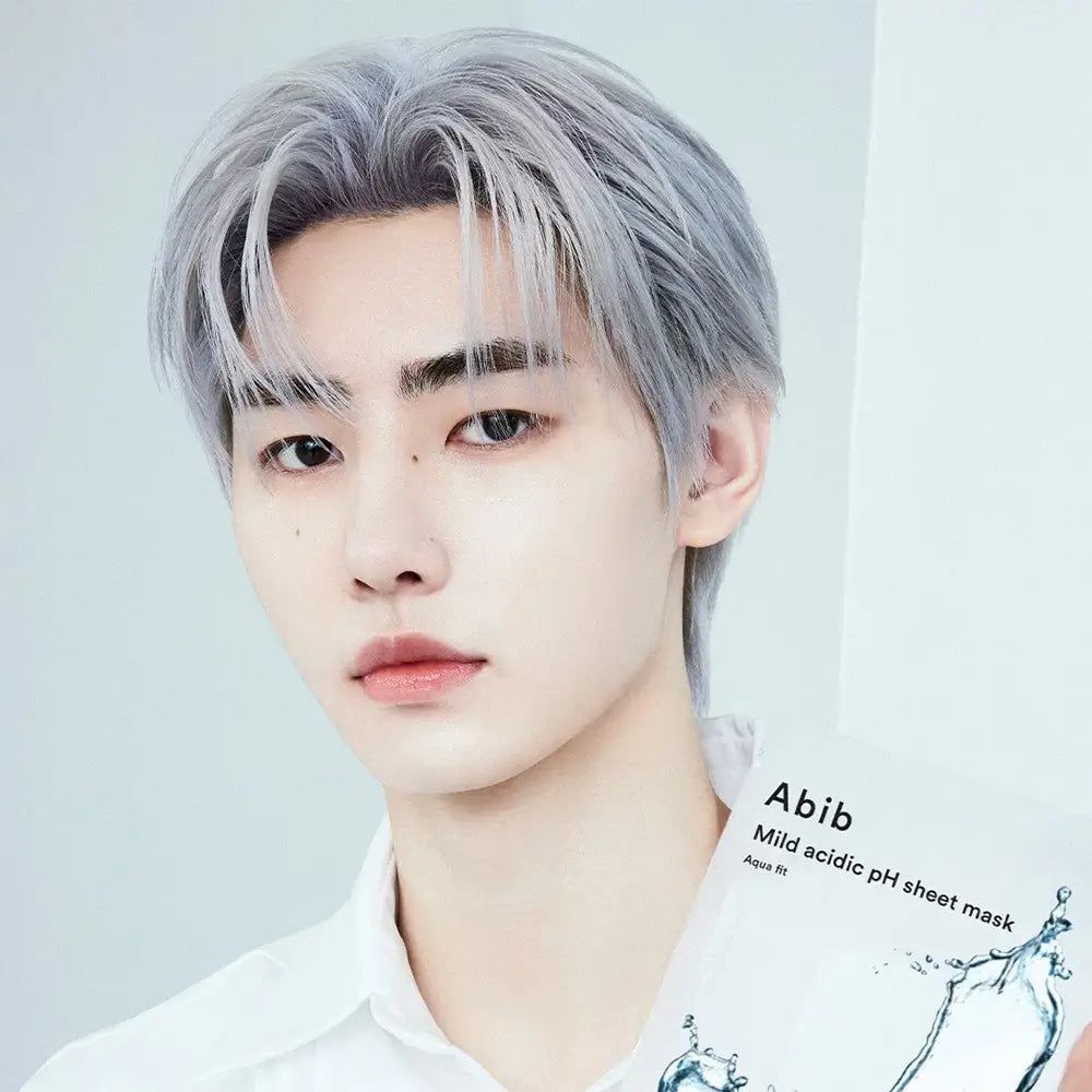 Personne tenant le masque facial ABIB Milde Säure pH Aqua Fit. Emballage du produit avec le nom du produit. Personne aux cheveux gris et chemise claire.